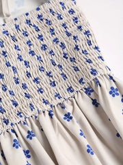 Close-up of the elastic smocking and blue floral pattern on a white dress bodice.