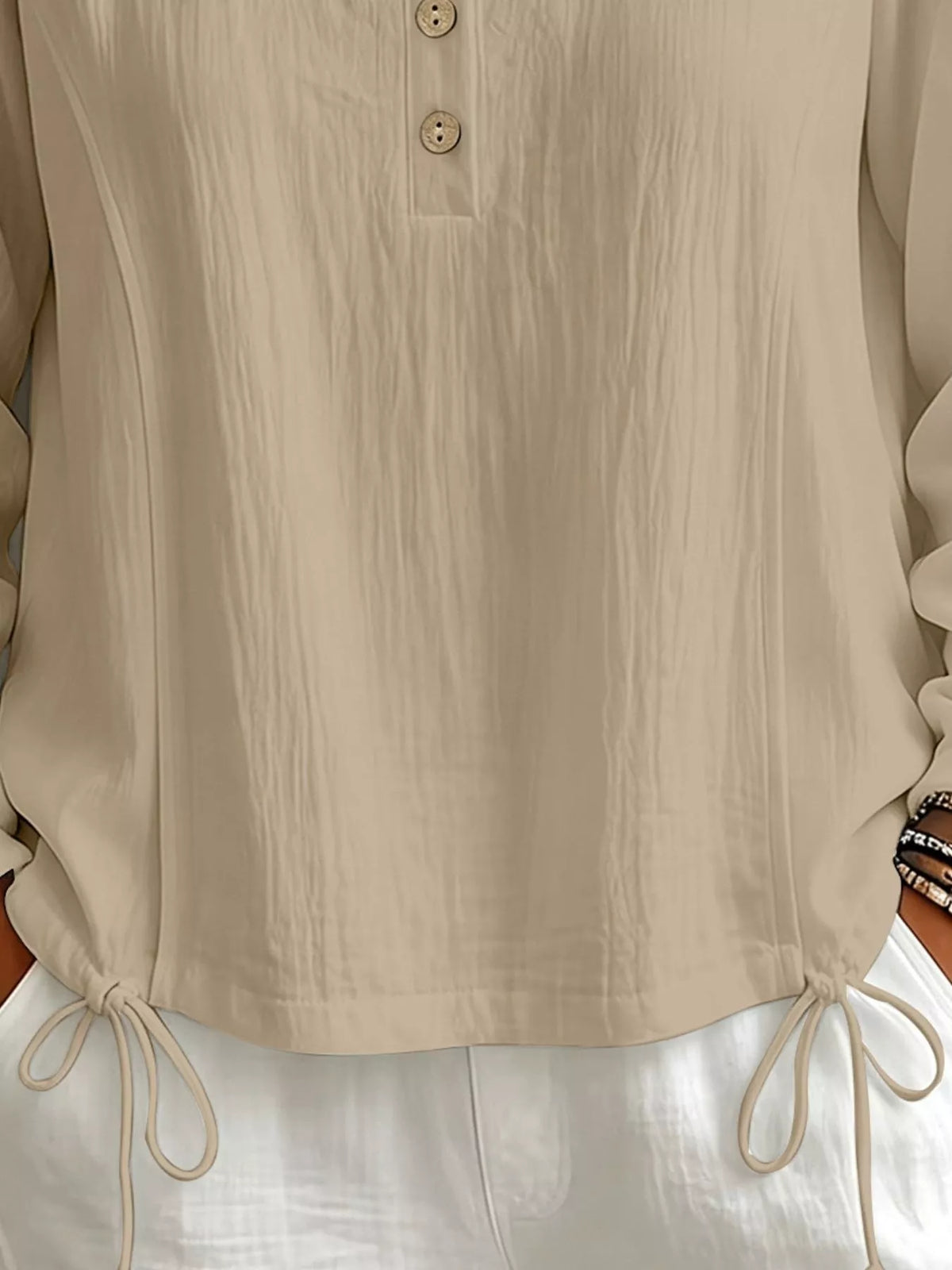 Close-up of the beige blouse showing its front buttons and adjustable drawstring hem.