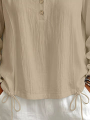 Close-up of the beige blouse showing its front buttons and adjustable drawstring hem.