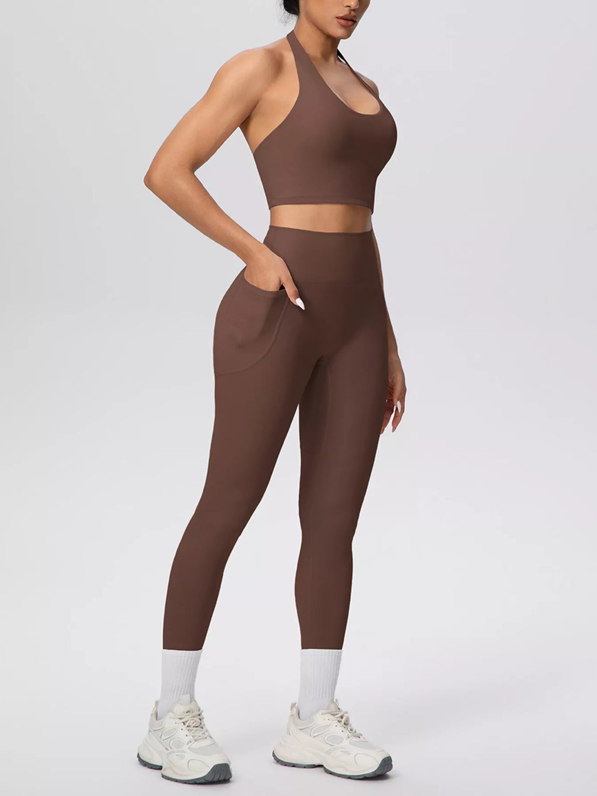 Model poses in brown halter activewear set with hand at waistband