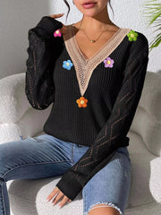 Seated view of the black floral sweater showing its openwork sleeve pattern.