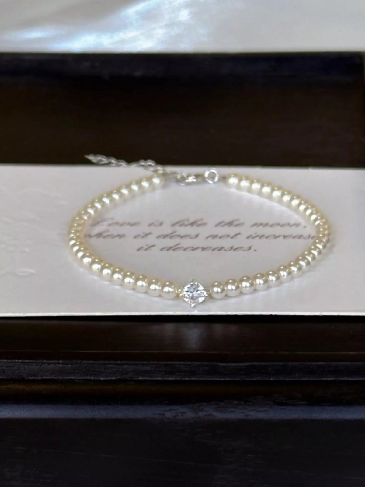 Pearl bracelet laid inside a dark jewelry box with a card beneath it.