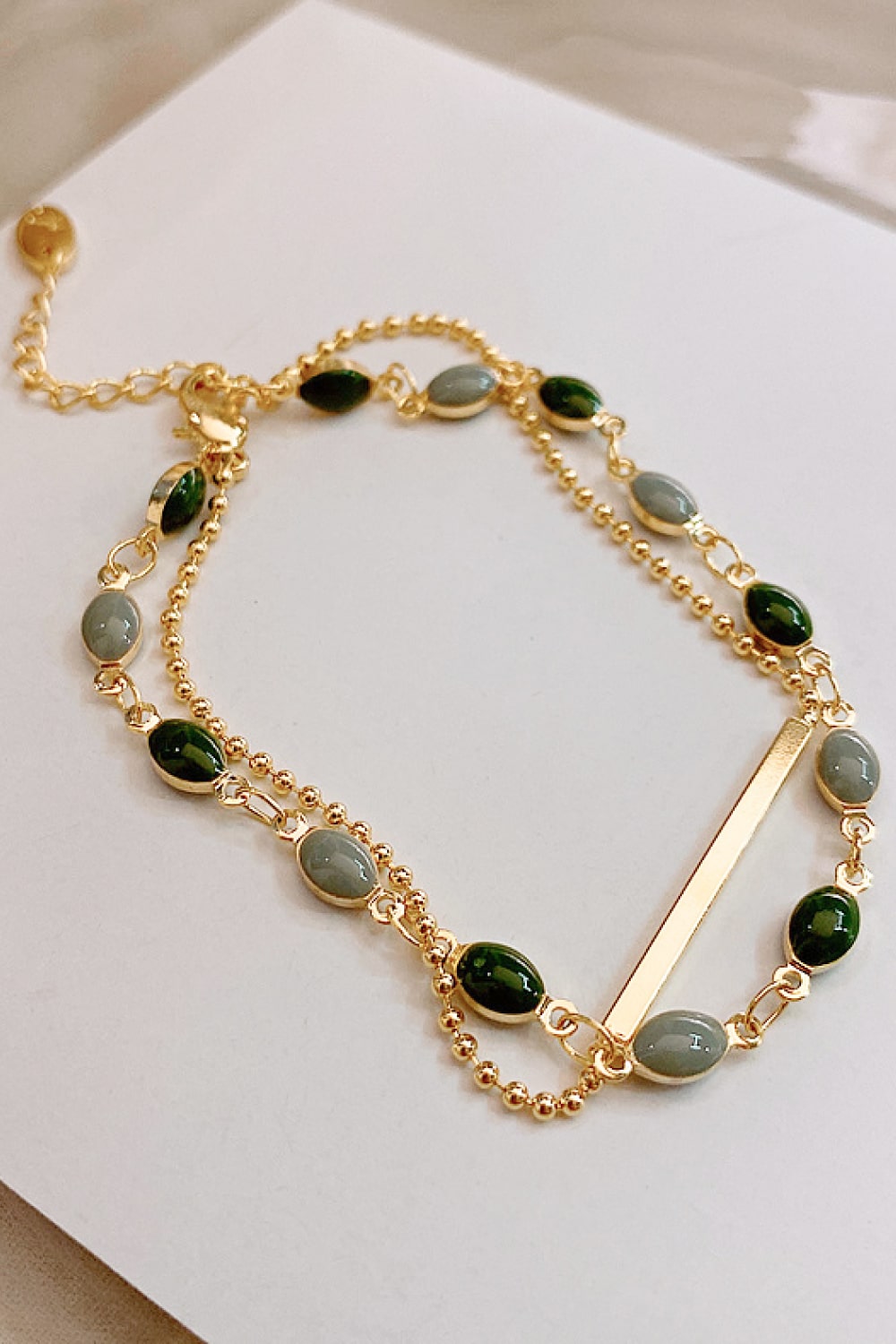 Close-up of two gold-tone chains and oval green and pale blue stones on a bracelet