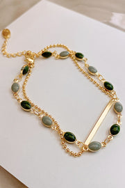 Close-up of two gold-tone chains and oval green and pale blue stones on a bracelet
