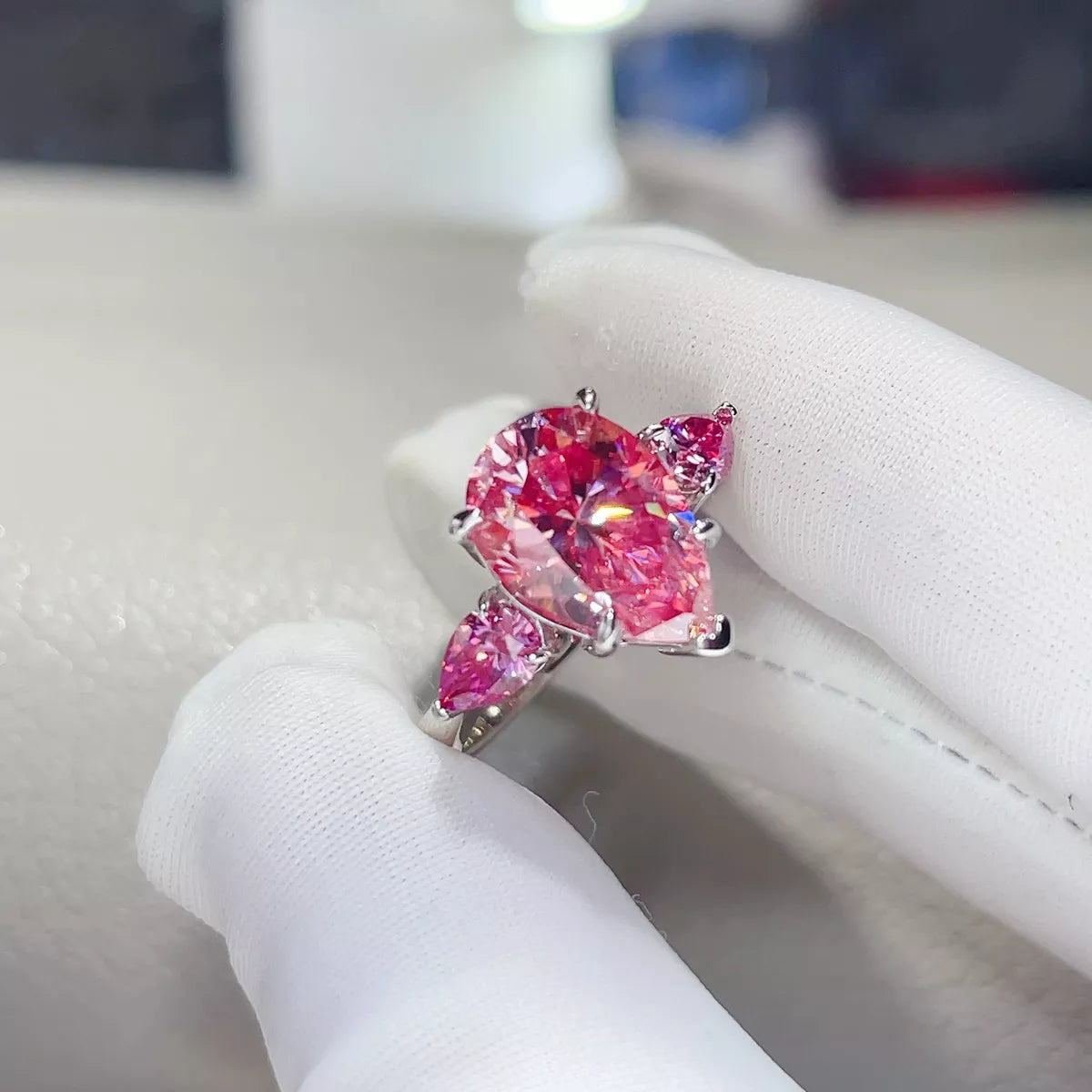Angled pink teardrop moissanite ring held in a gloved hand