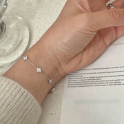 Silver four-leaf clover bracelet worn on wrist beside a card