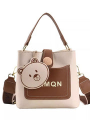 Front view of ivory mini bucket bag with brown pocket, top handle and bear charm