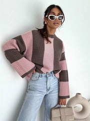 Model wearing the pink and brown sweater seated with one knee raised