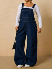 Dark blue wide-leg denim overalls with a bib pocket, full-length front view over a white long-sleeve top.