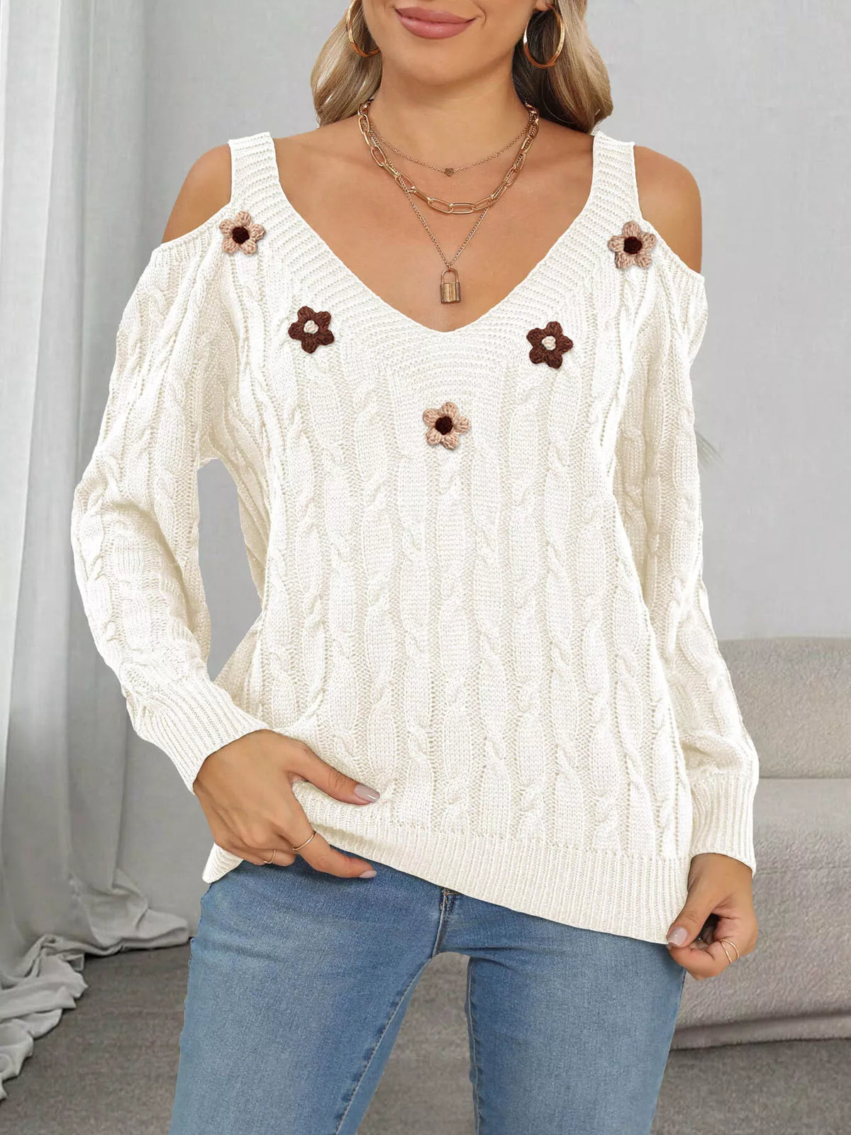 White cable-knit sweater with floral appliqués worn with jeans, front view
