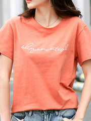 Coral short-sleeve T-shirt with white cursive lettering across the chest, shown on a model