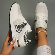 White wedge sneakers with black floral mesh panels, shown from above