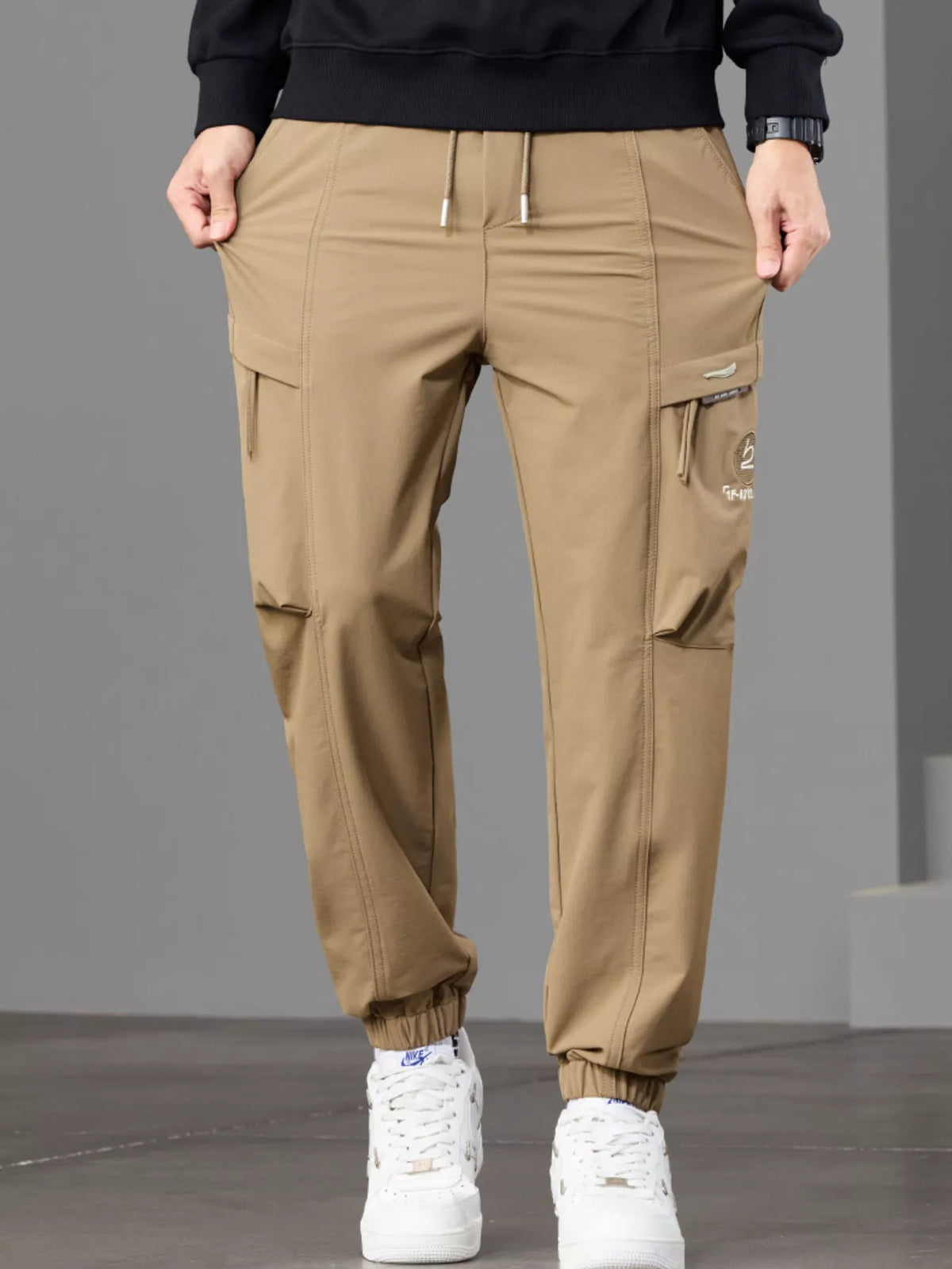 Close front view of tan joggers showing the drawstring waist and cargo pocket flaps.