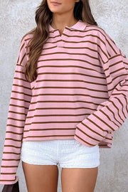Model wearing pink and brown striped collared long-sleeve top with white shorts.