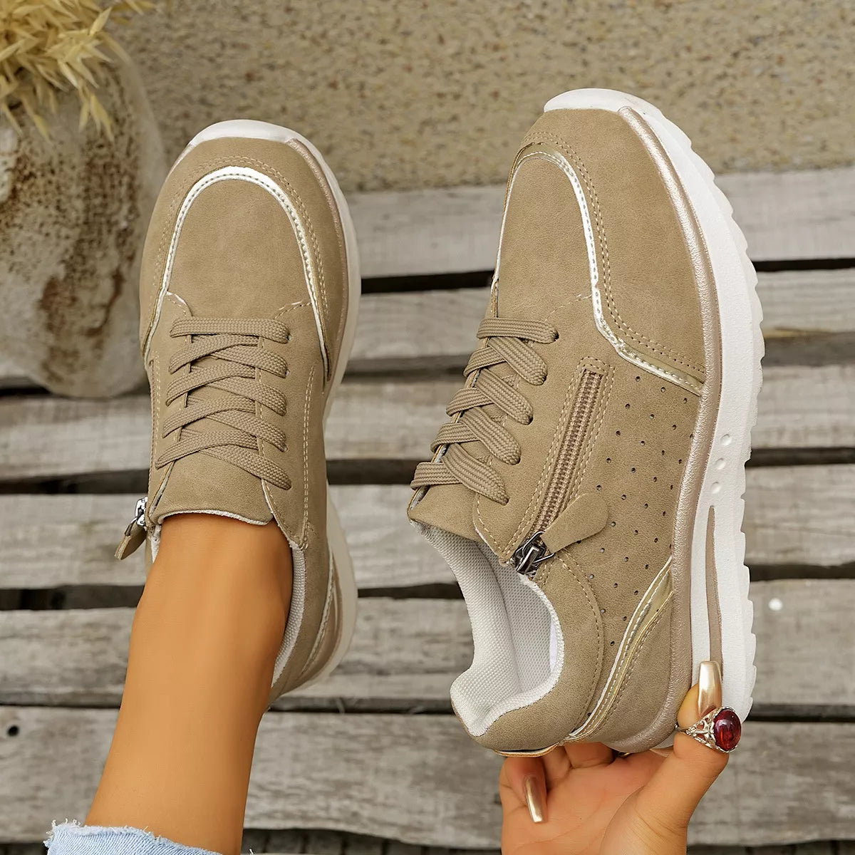 Taupe sneakers held to show their soles