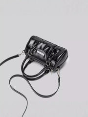 Top-down angled view of the black Boston bag with the long crossbody strap laid beside it.