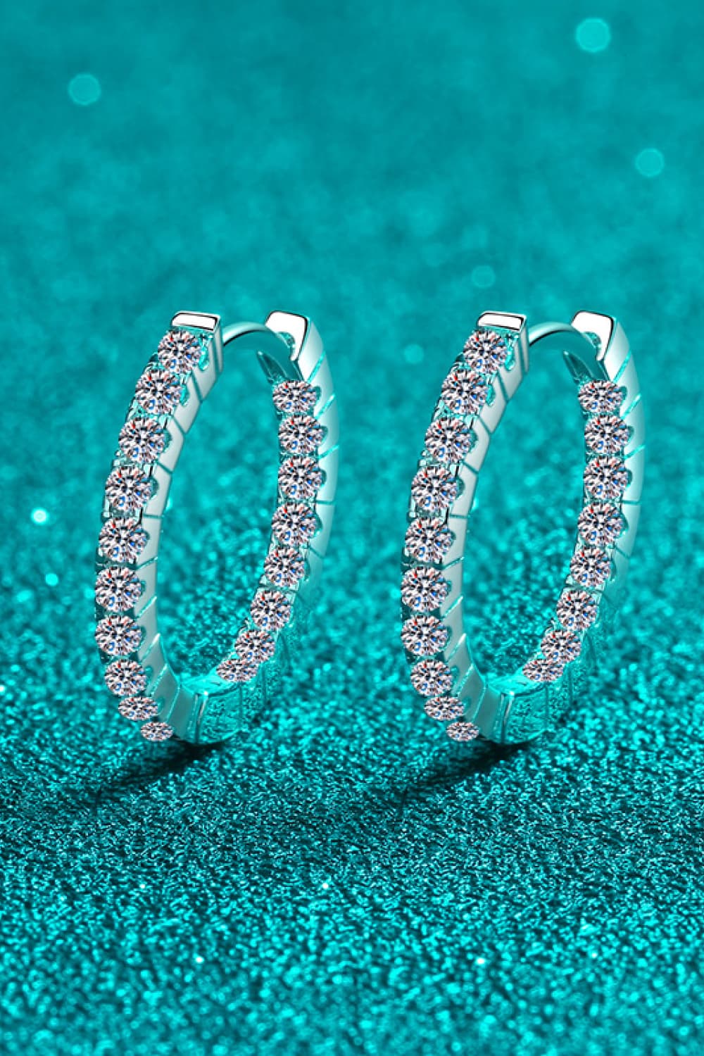 Moissanite 925 Sterling Silver Huggie Earrings — Angled view of moissanite huggie hoops on teal background