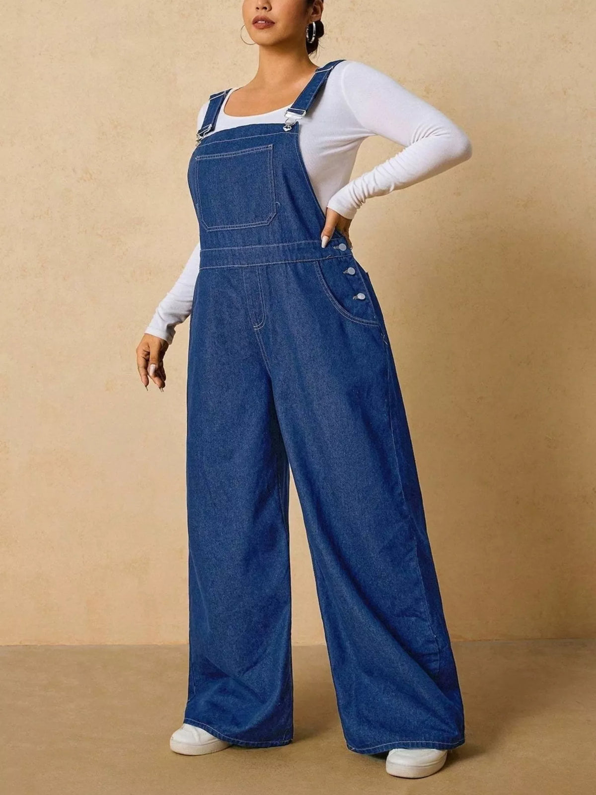 Angled view of medium blue denim overalls with one hand resting at the waist.