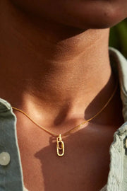 Close-up of gold-tone rectangular pendant necklace worn by a model