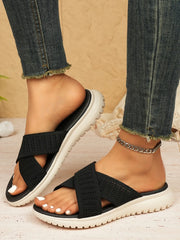 Black woven cross-strap sandals with contrasting white ridged soles, side view on feet