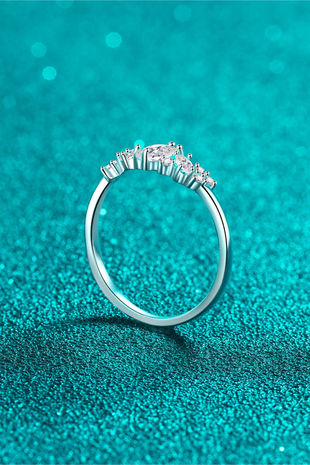 Rhodium-tone ring viewed from the back, showing its raised center setting against teal fabric