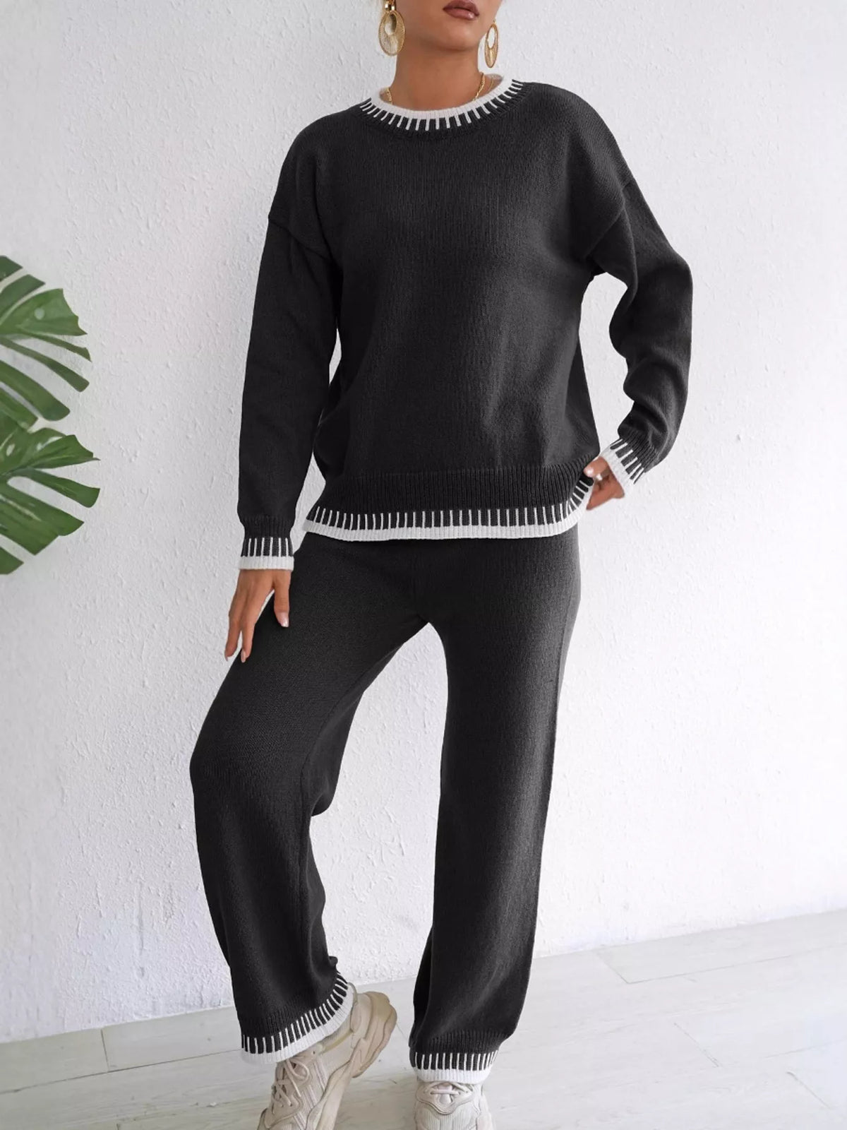 Front view of the black knit set with white contrast neckline, cuffs and hems, model leaning to one side.
