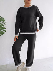 Front view of the black knit set with white contrast neckline, cuffs and hems, model leaning to one side.