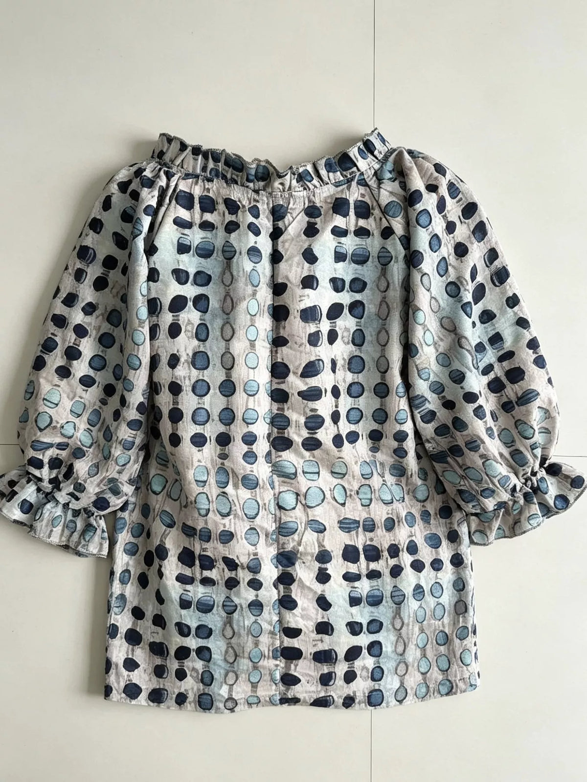 Back of the beige and blue printed blouse laid flat, showing gathered neckline.