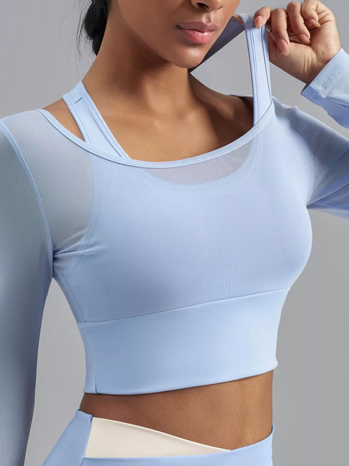 Model lifting the light blue inner shoulder strap to show the active top's built-in bra layer