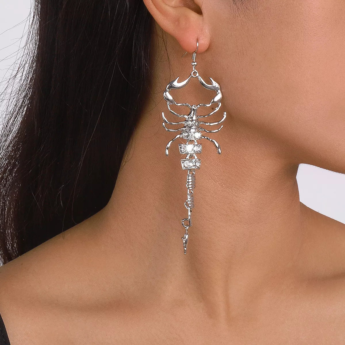 Silver-tone scorpion dangle earring worn on an ear, front view