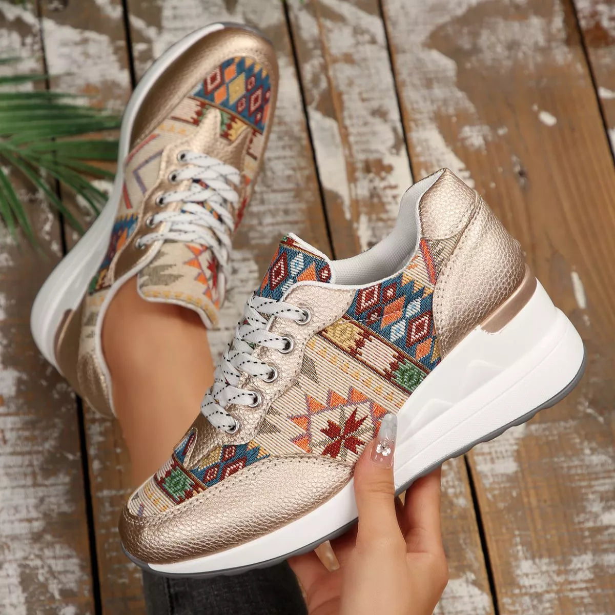 Top-down view of cream geometric-print wedge sneakers held in hand