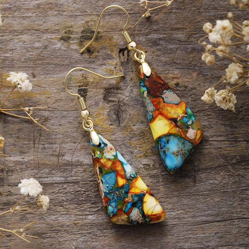 Pair of multicolour geometric drop earrings with gold-tone hooks on weathered wood