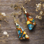 Pair of multicolour geometric drop earrings with gold-tone hooks on weathered wood