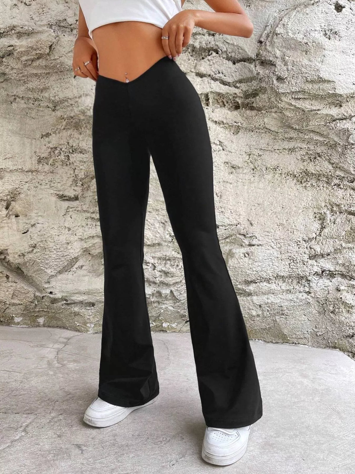 Angled front view of black V-waist flare pants, with hands holding the waistband.