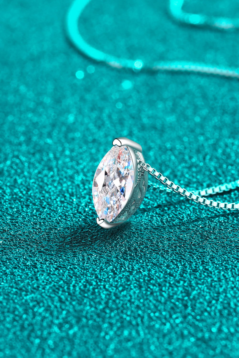 Side view of marquise-cut moissanite pendant on teal background