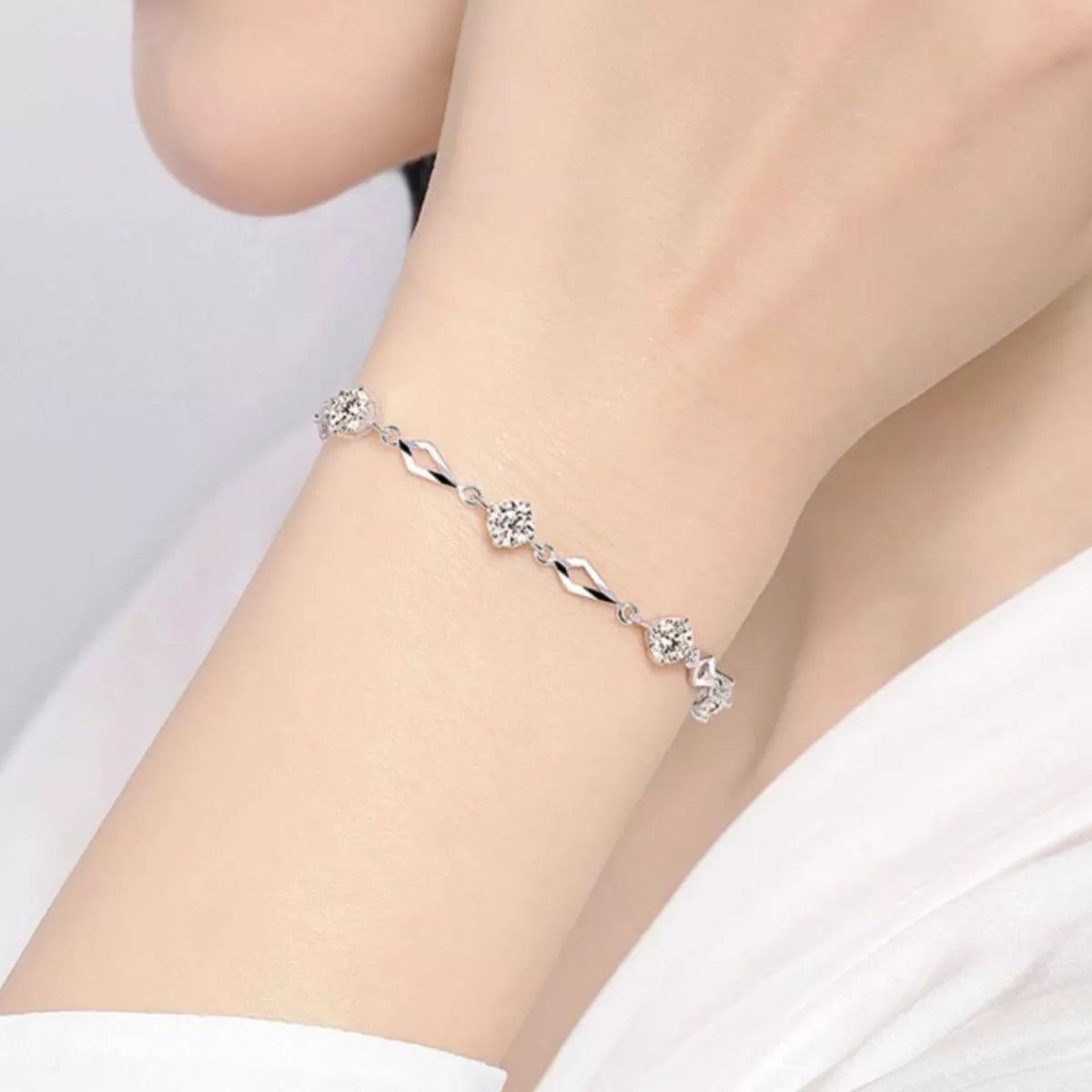 Wrist wearing a delicate silver-tone bracelet with wavy links and sparkling flower clusters