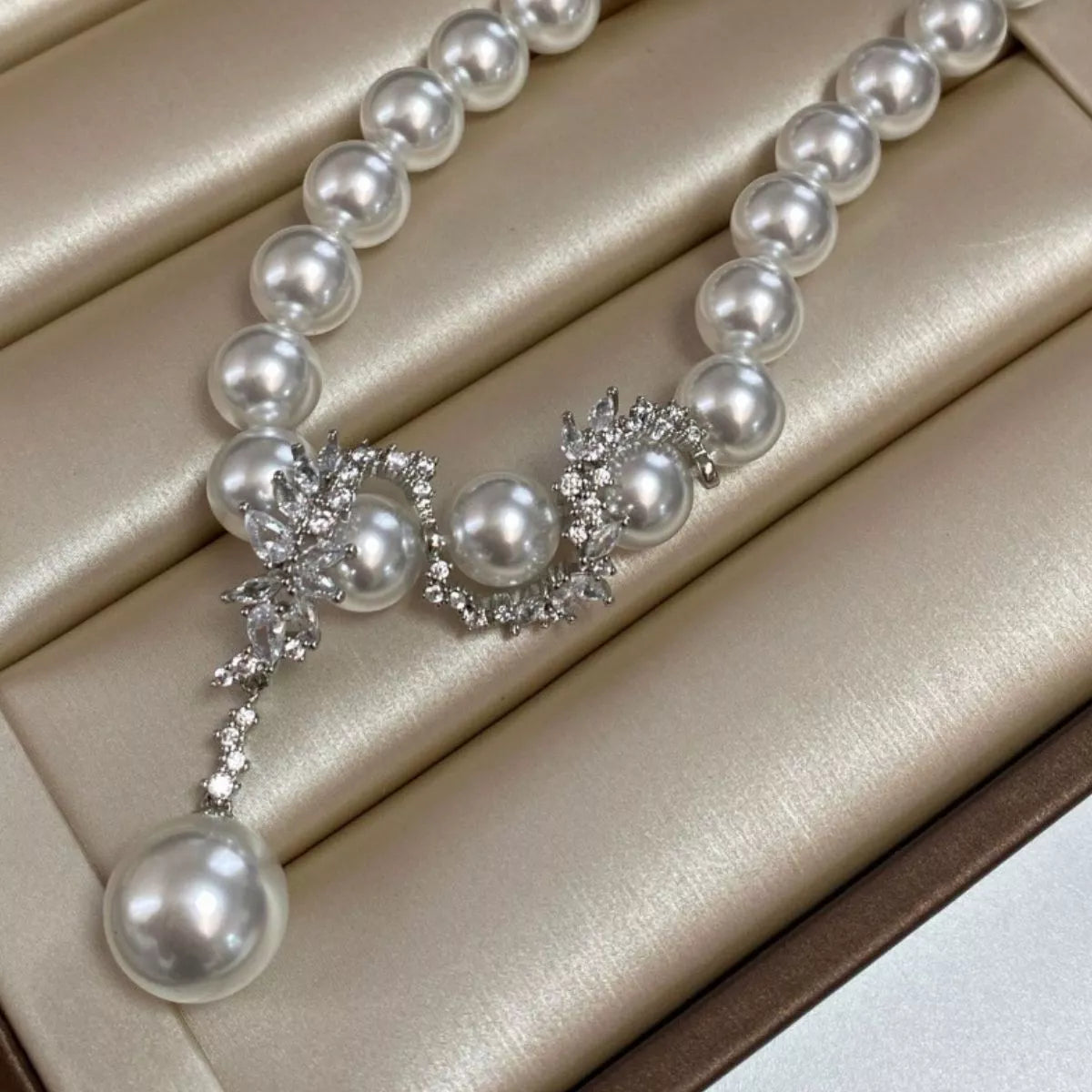 Pearl necklace and sparkling centerpiece displayed on folded champagne fabric