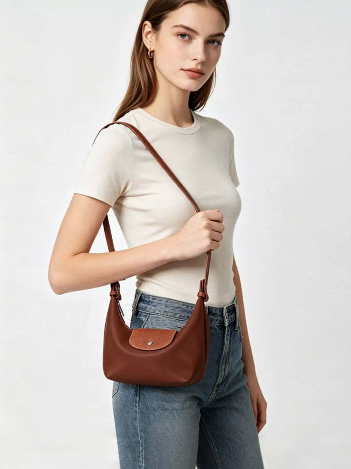 Model carrying the brown bag crossbody with its long strap and rounded body visible.