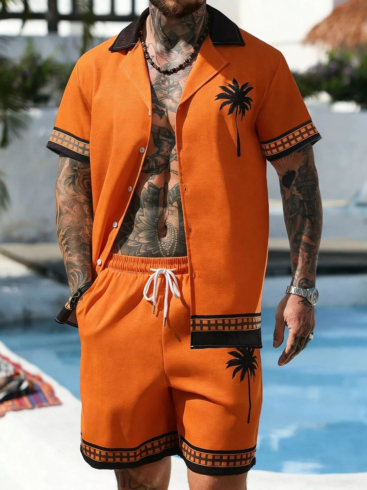 Model wearing orange palm-tree print shirt and matching shorts by a pool