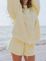 Pale yellow sweatshirt and matching drawstring shorts shown on a model with arms raised.