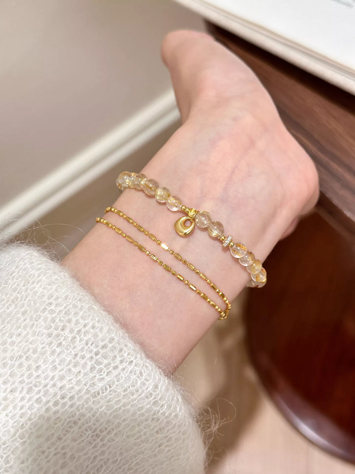 Close wrist view of a gold-plated bracelet with small bead and charm details.