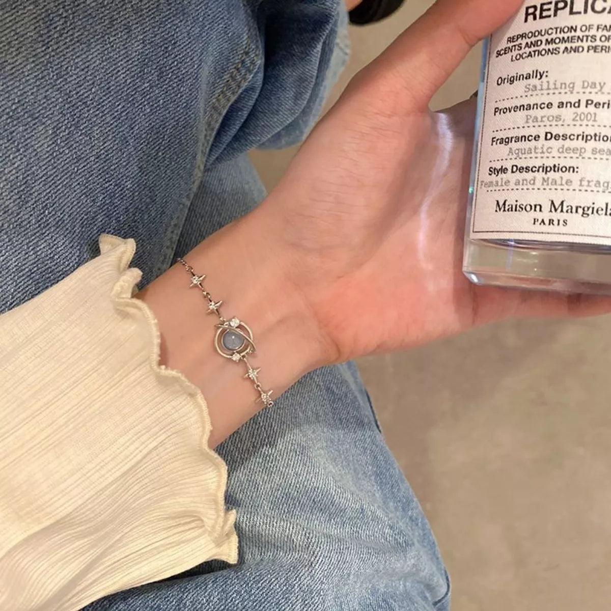 Silver planet bracelet shown in hand with a small perfume bottle for scale