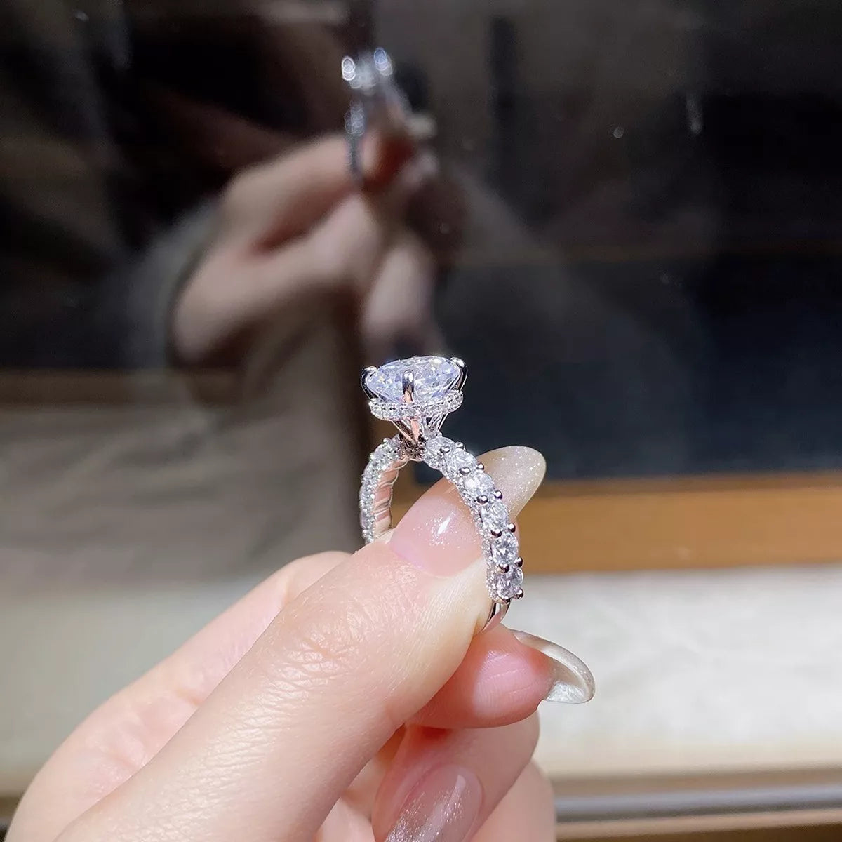 A hand holds the ring to show its raised round stone and decorated band.