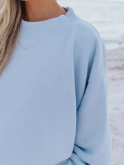 Close-up of the crewneck and dropped shoulder on a light blue sweatshirt.