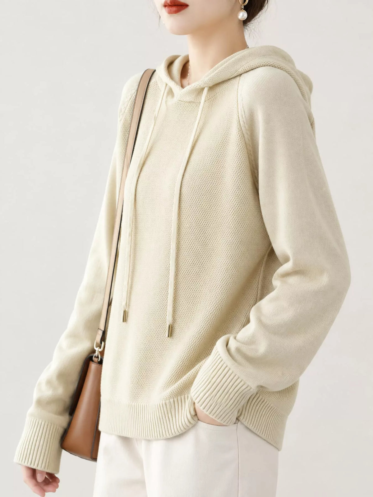 Angled view of the cream hooded sweater with one hand in a trouser pocket.