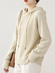 Angled view of the cream hooded sweater with one hand in a trouser pocket.