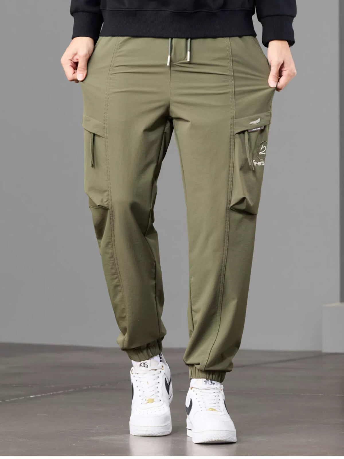 Close front view of olive joggers showing the cargo pocket and waist drawstring.