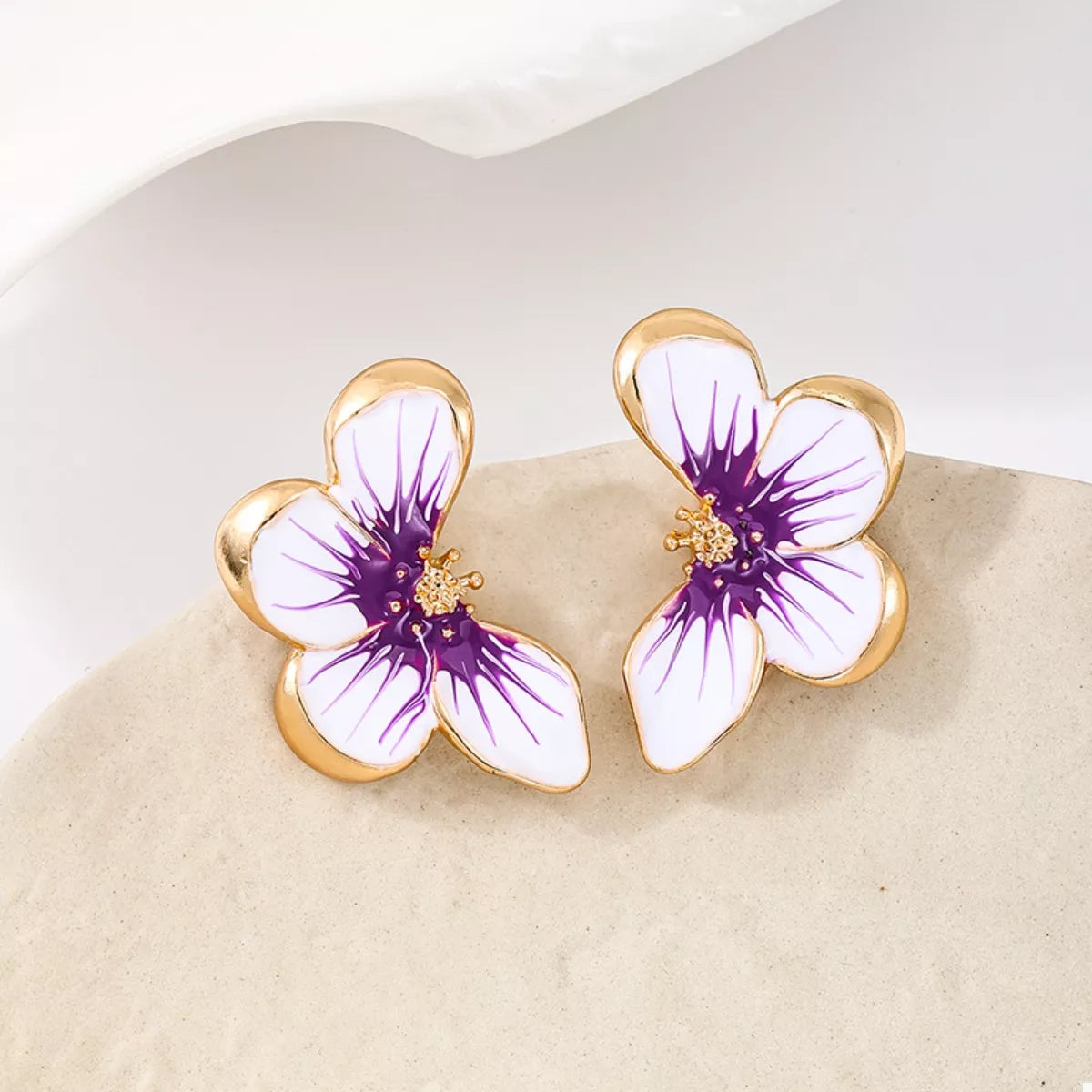 Pair of purple-and-white flower studs resting on a pale stone