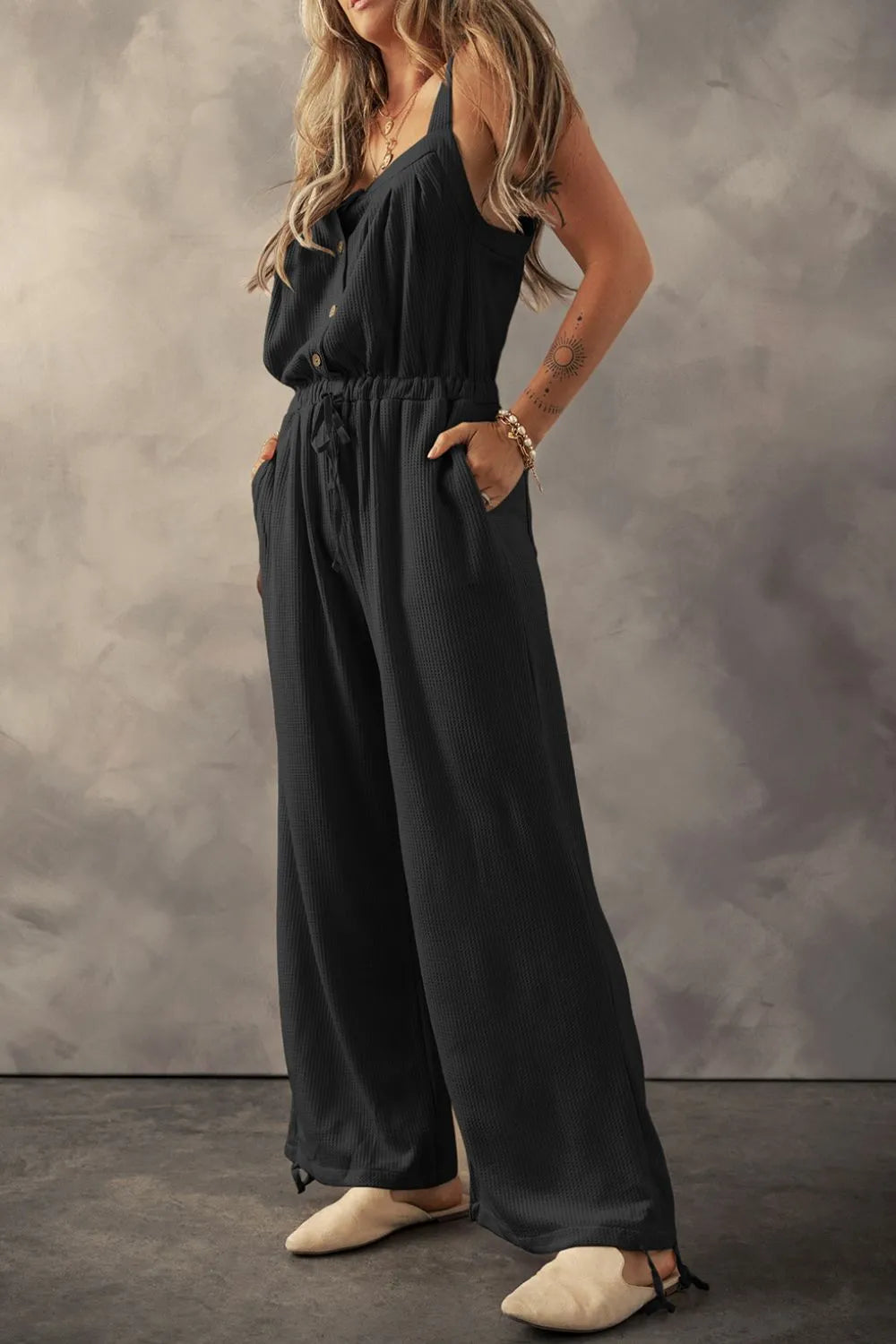 Black textured jumpsuit with knotted straps, model angled side pose