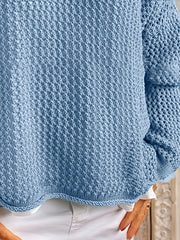 Lower front of a blue open-knit cover-up showing its hem and long sleeve above white shorts.